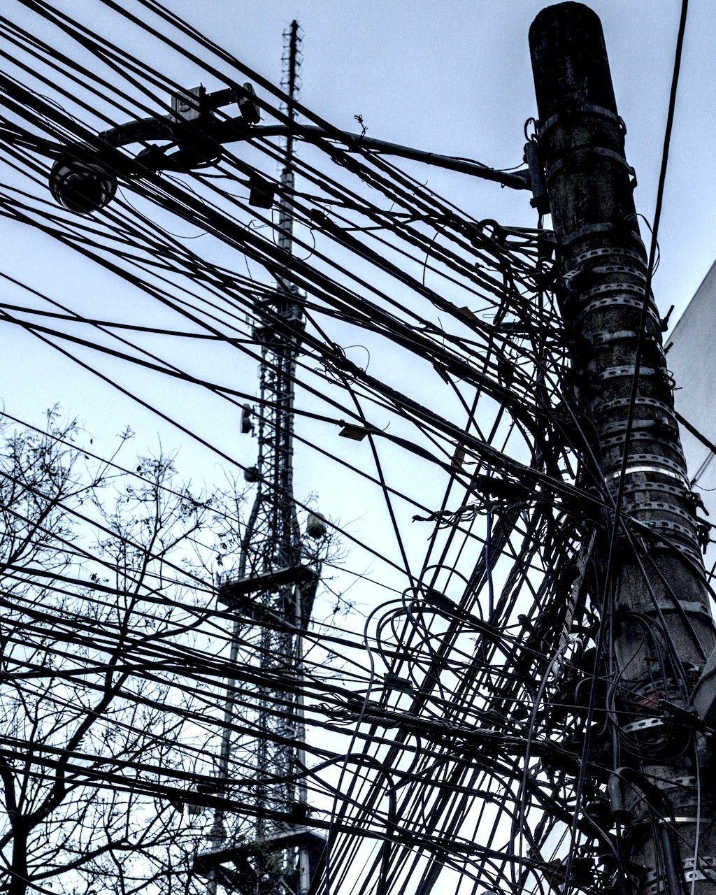 Torre de telecomunicação ao funde escondida por fios de poste em primeiro plano.
