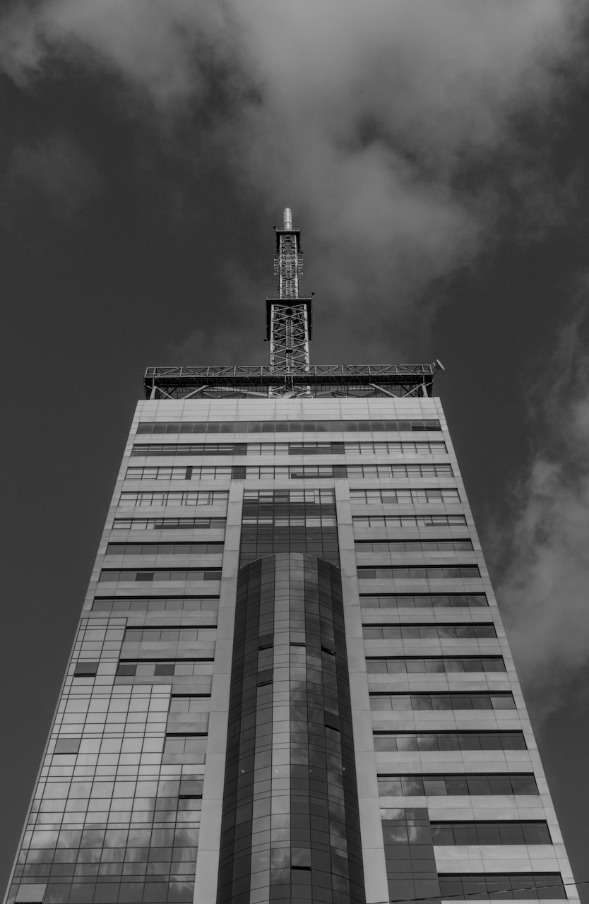 Contra-plongée de torre metálica sobre prédio envidraçado.