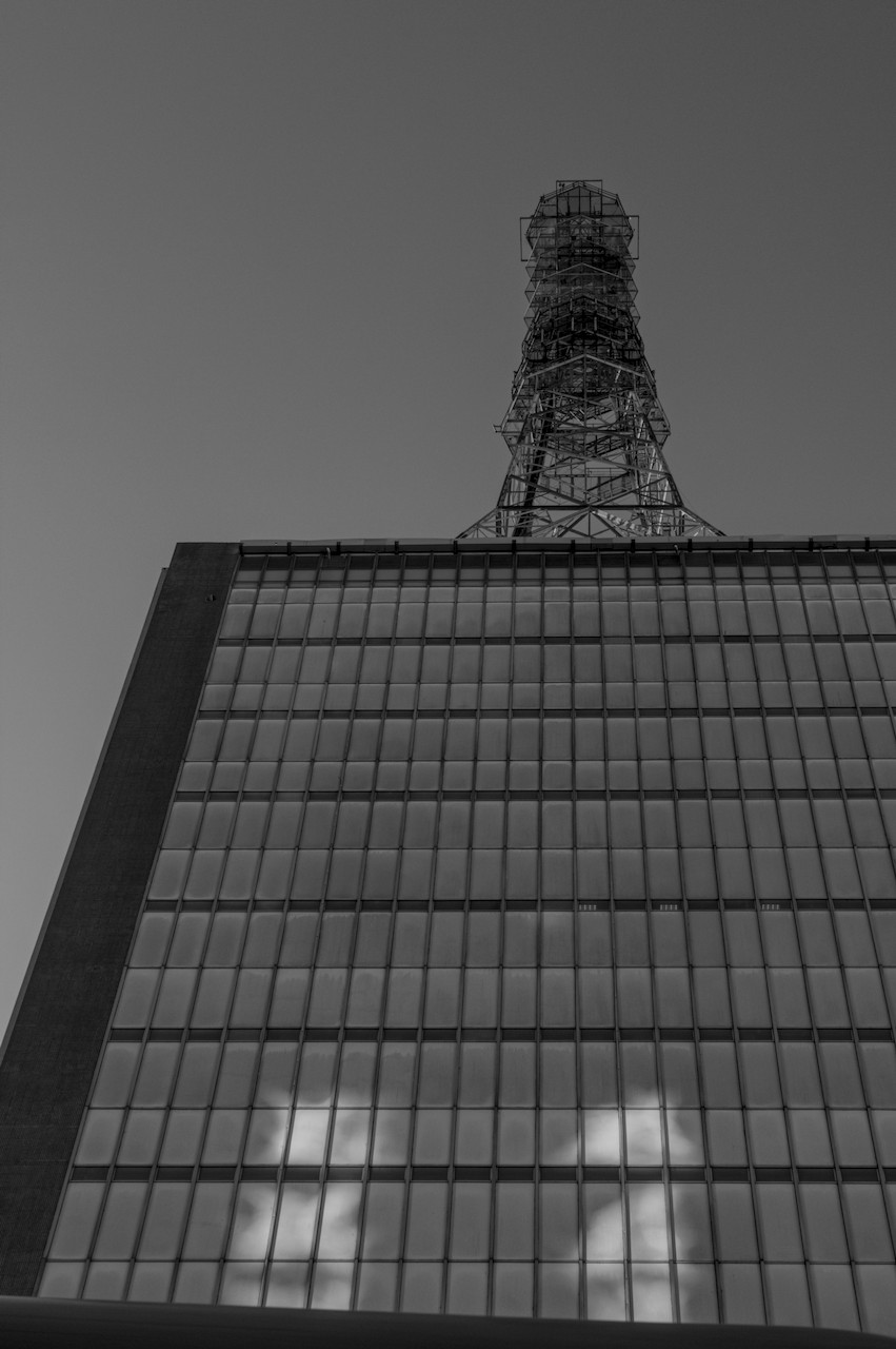 Contra-plongée de torre metálica cilíndrica sobre prédio envidraçado.