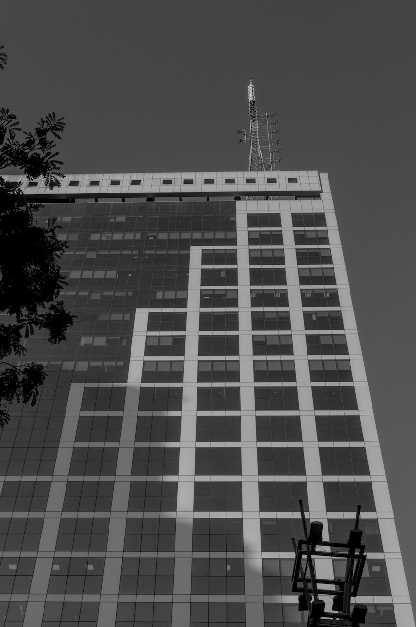 Contra-plongée de torre metálica à direita sobre prédio envidraçado com formas geométricas.