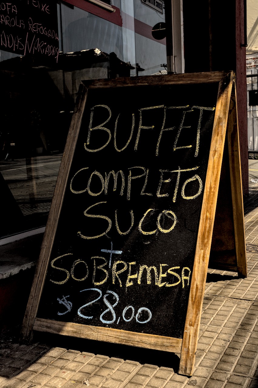 Lousa sob Sol duro com a frase 'Buffet Completo Suco + Sobremesa $28,00'.
