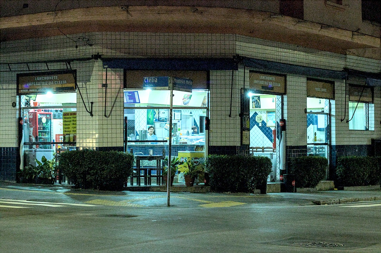 Boteco de esquina sob a luz da madrugada; mulher ao balcão.